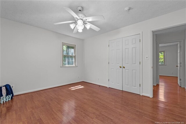 unfurnished bedroom with hardwood / wood-style flooring, a closet, ceiling fan, and multiple windows