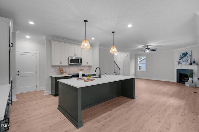 kitchen with an island with sink, white cabinetry, a fireplace, appliances with stainless steel finishes, and ceiling fan