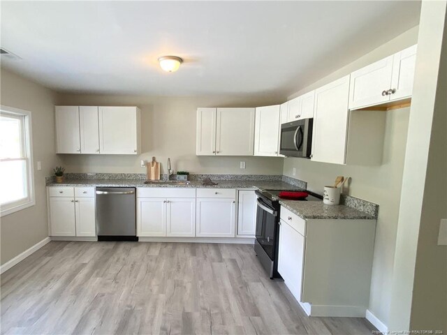 kitchen featuring sink, light hardwood / wood-style floors, white cabinetry, dark stone counters, and stainless steel appliances