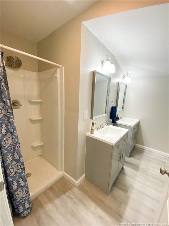 bathroom featuring vaulted ceiling, wood-type flooring, dual vanity, and a shower with curtain