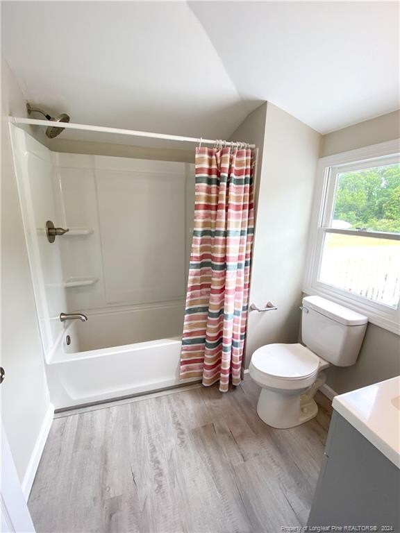 full bathroom with wood-type flooring, vanity, shower / bath combination with curtain, and toilet