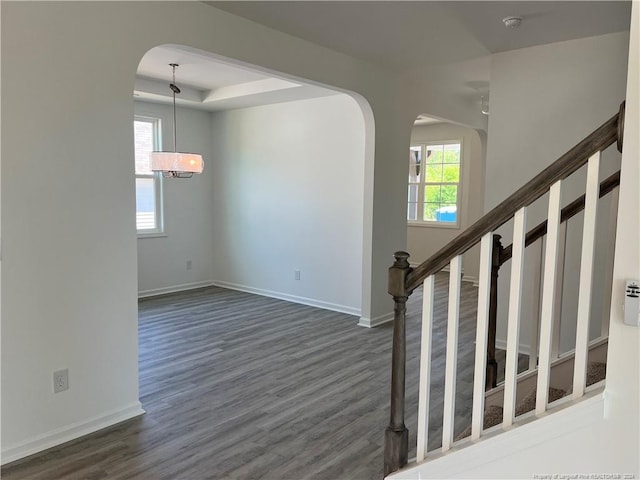 stairs with wood-type flooring, a raised ceiling, and plenty of natural light