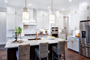 kitchen featuring custom exhaust hood, dark hardwood / wood-style flooring, appliances with stainless steel finishes, and an island with sink