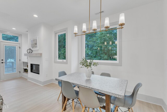 dining space featuring plenty of natural light, light wood-style flooring, visible vents, and a glass covered fireplace