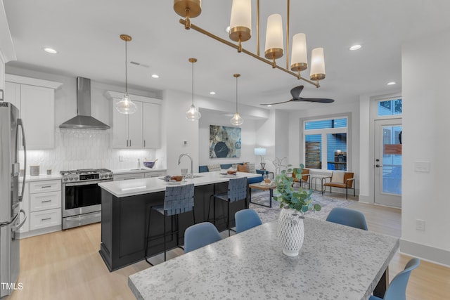 kitchen featuring a center island with sink, a breakfast bar area, open floor plan, stainless steel appliances, and wall chimney range hood