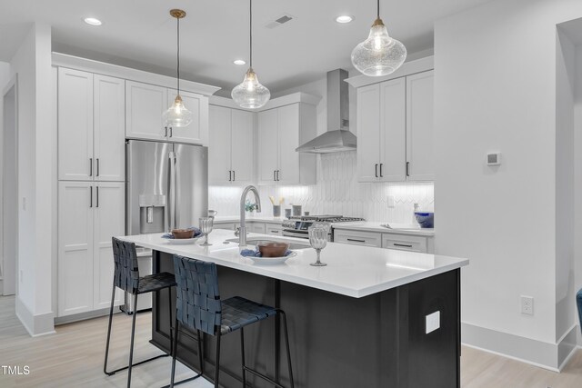 kitchen with decorative backsplash, wall chimney exhaust hood, appliances with stainless steel finishes, a kitchen bar, and a sink