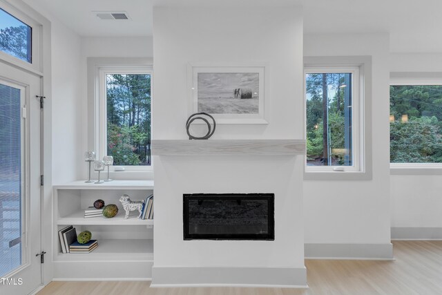 interior details with a glass covered fireplace, visible vents, baseboards, and wood finished floors