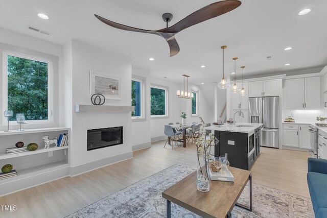 living area featuring recessed lighting, visible vents, baseboards, light wood-style floors, and a glass covered fireplace