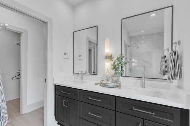 full bath with wood finished floors, a sink, a marble finish shower, and double vanity