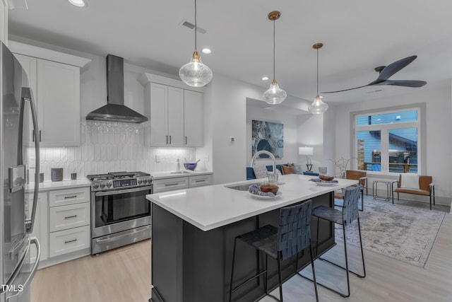 kitchen featuring white cabinetry, sink, wall chimney exhaust hood, stainless steel appliances, and an island with sink