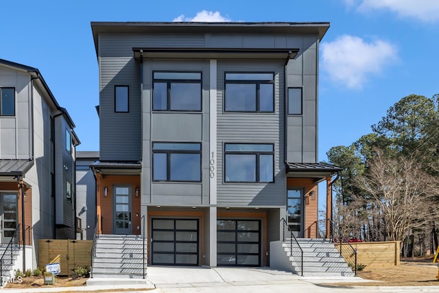 contemporary home featuring concrete driveway, metal roof, an attached garage, a standing seam roof, and fence