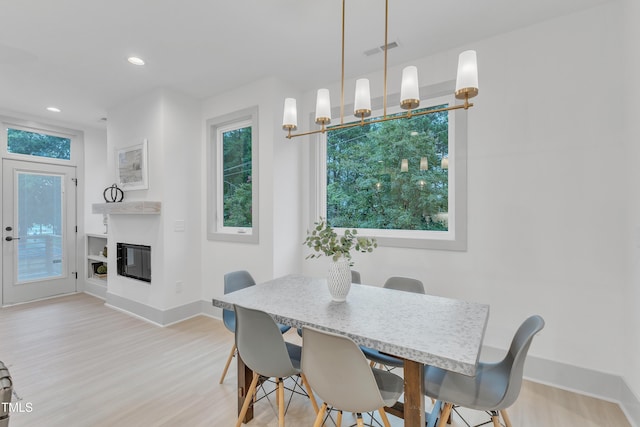 dining room featuring a wealth of natural light, a glass covered fireplace, visible vents, and light wood-style floors