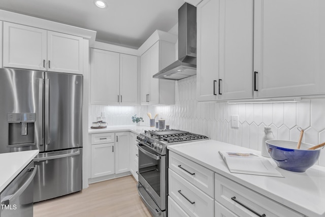 kitchen with tasteful backsplash, white cabinets, stainless steel appliances, light countertops, and wall chimney range hood