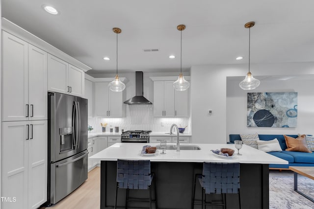 kitchen featuring a sink, open floor plan, appliances with stainless steel finishes, wall chimney range hood, and tasteful backsplash