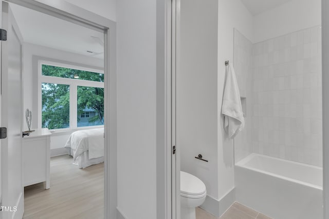 ensuite bathroom with baseboards, toilet, ensuite bath, wood finished floors, and bathtub / shower combination