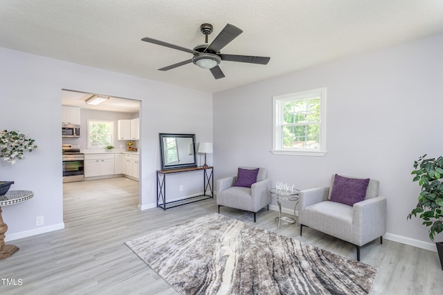 living area with plenty of natural light, ceiling fan, light hardwood / wood-style floors, and a textured ceiling