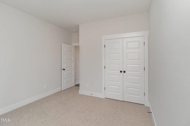 unfurnished bedroom featuring light carpet, a closet, and baseboards