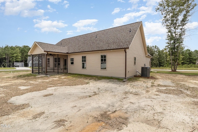 rear view of house with central air condition unit, a sunroom, and roof with shingles