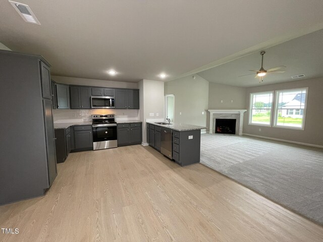 kitchen with gray cabinets, ceiling fan, stainless steel appliances, light stone countertops, and light colored carpet