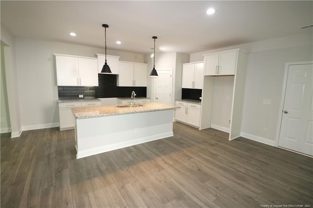 kitchen with white cabinets, a kitchen island with sink, dark hardwood / wood-style floors, light stone counters, and tasteful backsplash