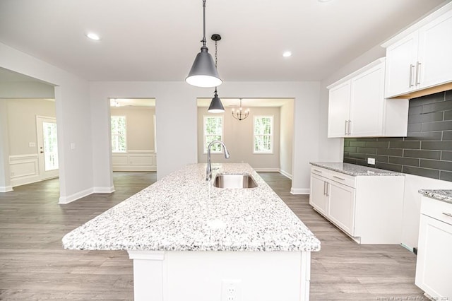 kitchen featuring wood-type flooring, backsplash, hanging light fixtures, sink, and a kitchen island with sink