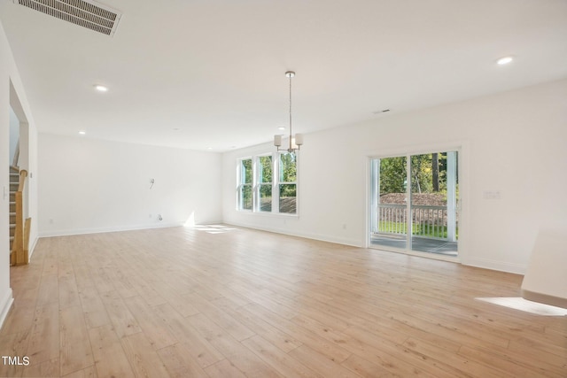 unfurnished living room with a wealth of natural light, light hardwood / wood-style flooring, and a chandelier