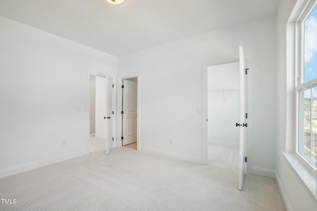 unfurnished bedroom with a walk in closet, multiple windows, and light colored carpet