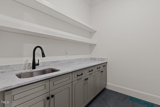 bar with dark tile patterned flooring, sink, gray cabinets, light stone countertops, and ornamental molding