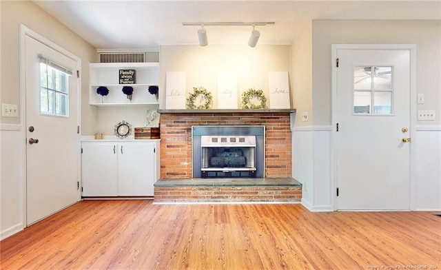 interior space with light hardwood / wood-style floors, a brick fireplace, and track lighting