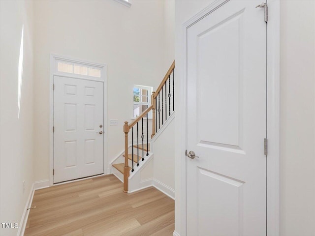 foyer with a high ceiling, light wood-style flooring, baseboards, and stairs