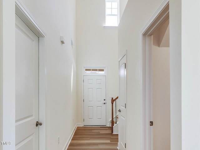 corridor featuring a high ceiling, light wood-type flooring, and baseboards