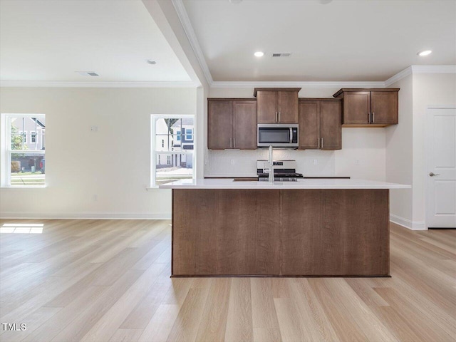 kitchen with a sink, light wood-style floors, light countertops, stainless steel microwave, and a center island with sink