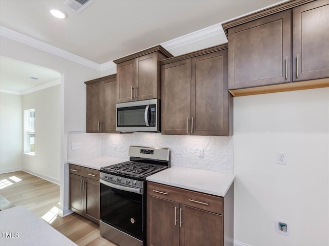 kitchen with tasteful backsplash, visible vents, light wood-style flooring, appliances with stainless steel finishes, and ornamental molding