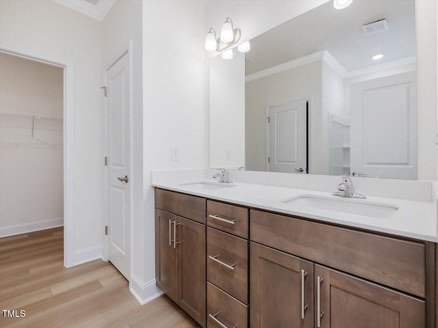 bathroom featuring wood finished floors, ornamental molding, a sink, and visible vents