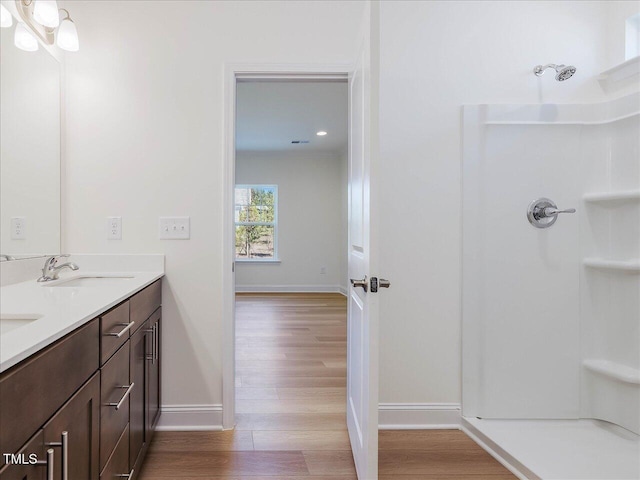 full bath featuring a shower, double vanity, a sink, wood finished floors, and baseboards