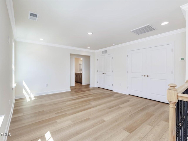 unfurnished bedroom featuring crown molding, light wood-style floors, visible vents, and multiple closets