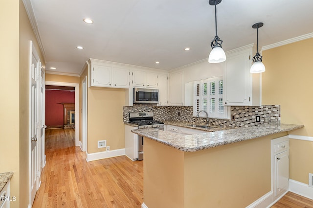 kitchen with appliances with stainless steel finishes, sink, light stone counters, white cabinetry, and kitchen peninsula