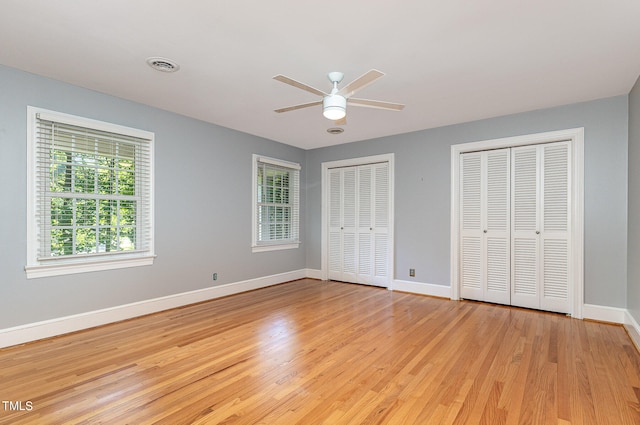 unfurnished bedroom featuring light wood-type flooring, multiple closets, and ceiling fan