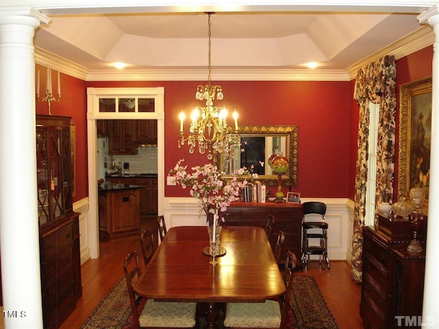 dining space with a raised ceiling, ornate columns, hardwood / wood-style flooring, and a notable chandelier