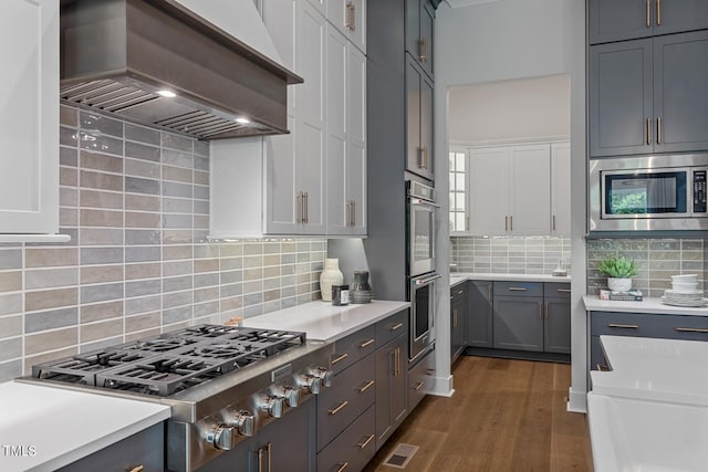 kitchen with white cabinets, backsplash, dark hardwood / wood-style flooring, stainless steel appliances, and custom range hood