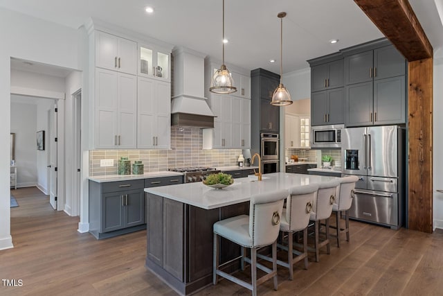 kitchen with custom exhaust hood, dark hardwood / wood-style floors, appliances with stainless steel finishes, a center island with sink, and tasteful backsplash