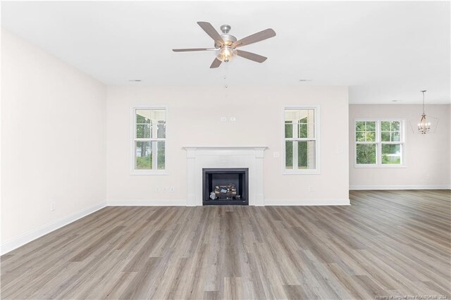 unfurnished living room featuring light hardwood / wood-style flooring, ceiling fan with notable chandelier, and plenty of natural light