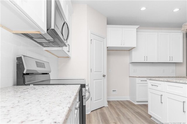 kitchen featuring light stone countertops, light wood-type flooring, stainless steel appliances, and white cabinetry