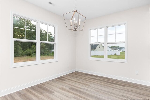 unfurnished room featuring light wood-type flooring, a chandelier, and a healthy amount of sunlight