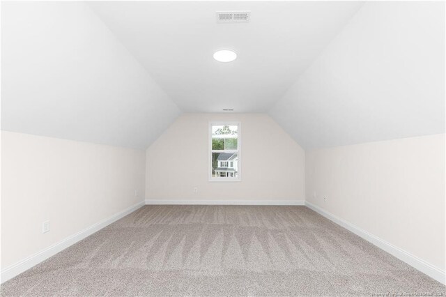 additional living space featuring vaulted ceiling and light colored carpet