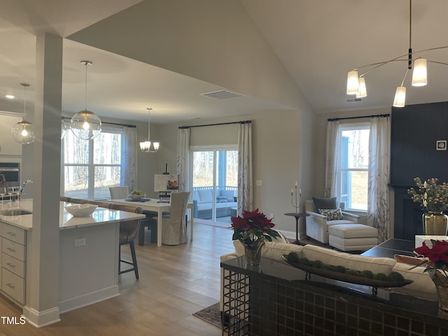 living room featuring a wealth of natural light, vaulted ceiling, sink, light hardwood / wood-style flooring, and a chandelier