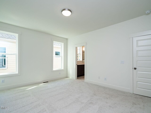 unfurnished bedroom featuring connected bathroom and light carpet