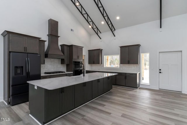 kitchen featuring a towering ceiling, light hardwood / wood-style flooring, a kitchen island, backsplash, and premium range hood