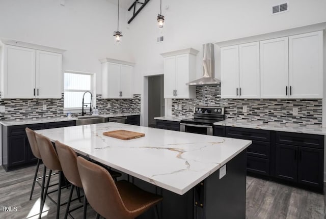 kitchen featuring a center island, wall chimney range hood, stainless steel electric stove, and backsplash