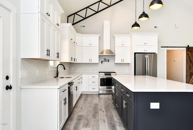 kitchen with stainless steel appliances, pendant lighting, wall chimney exhaust hood, sink, and white cabinetry